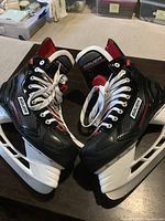 Pair of black Bauer ice hockey skates with white laces and blades shown side by side on carpeted floor.