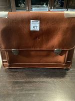 Front view of the tan brown leather briefcase showing the front flap, branding, and clasps.