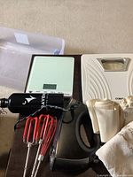 Photo of the Conair analog bathroom scale, digital kitchen scale, and black hand mixer with red beaters all together on a brown surface.