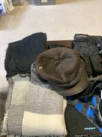 Scarves, brown leather caps, and gloves arranged on a wooden surface and carpet