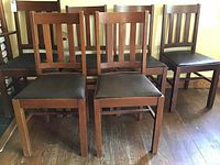 Photo showing six matching antique wooden chairs with black padded seats, arranged in two rows on a wooden floor under yellow walls.