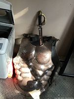 Full view of rusted metal breast plate with sword positioned behind it.