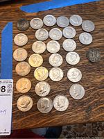 Full view of the 27 US half dollar coins laid out on wooden surface. Coins include a mix of Kennedy half dollars, bicentennial coins, and an older walking liberty coin.