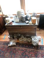 Wide view of all items on rustic wooden chest and floor, including ceramic crock, timers, tea kettles, glass jars, metal containers, and shakers.