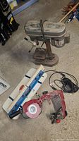 Full image of Duracraft drill press, rocker router table, red Rotozip spiral saw, and chain sharpener arrayed on the ground showing wear and dust