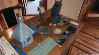 Various items on a wooden surface including a gray birdhouse, crystals, a welcome plaque, and evil eye keychain charms.