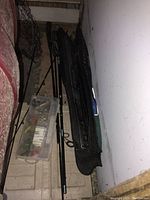 Photo showing fishing poles beside a black soft carrying case and a plastic tackle box on a white chest.