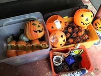 Photo showing multiple Jack o' Lantern plastic pumpkins and string lights inside storage bins along with other items