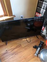 Full front view of the Hisense 44 inch TV sitting on the floor, black screen reflecting surroundings.
