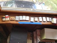 Wide view of all fourteen lighters lined up on a wooden windowsill showing varied sizes and colors including a large black and cream lighter marked 'Made in Occupied Japan'.