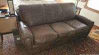 Front view of the brown leather Klaussner sofa showing the three seat cushions and rolled arms.