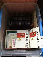 Plastic tote view showing three dark, hardcover stamp binders and assorted envelopes including first day covers with stamps.