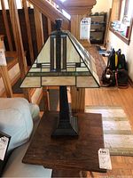 Full view of lamp showing the geometric stained glass shade with cream, white, and green accents, and dark metal base on a wooden table.