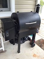 Full view of black barrel-style Traeger smoker on legs with side hopper and wheels