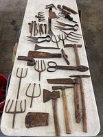 Overview of all antique tools spread on a white surface showing hatchets, gig heads, snips, large blades, and spikes.