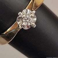 Close-up view of the small diamond set in a white gold or platinum-style flower-shaped setting on the yellow gold band showing detail of the prongs and gemstone.