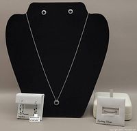 Sterling silver necklace with sapphire pendant, paired with stud and oval earrings, ring displayed alongside white jewellery box.