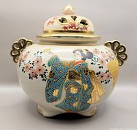 Front view showing detailed hand painted image of woman in blue kimono, floral decorations, sculpted gold-tone handles and lid with heart cutouts.
