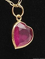 Close-up of heart-shaped ruby pendant in gold bezel against black background