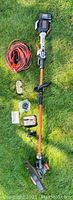Overall layout of the weed whacker and accessories on the grass showing the main tool, battery, charger, goggles, string spool, extension cord, and additional components.