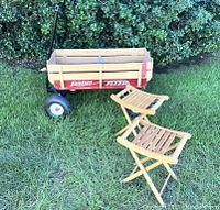 Photo showing the Radio Flyer wagon with wood sides and two wooden garden stools on grass with shrubbery background.