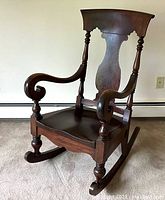 Side angle view showcasing the chair's sculpted arms, crest rail and turned front legs on rockers.