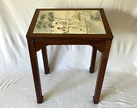Full frontal view of Chippendale-style wooden table with inset hand-painted Asian tiles on top showing two ladies and a natural landscape scene.