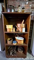 Full view of dark stained hardwood open cabinet shelving with various wooden boxes, pin cushion, oil lamp, jug, and lighting hardware grouped on shelves.