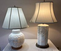 Both lamps lit on table against neutral background, round lamp on left, columnar lamp on right