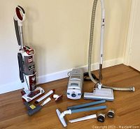 Shark upright and Electrolux canister vacuums with multiple loose attachments on floor