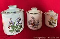 Three white ceramic canisters with floral and butterfly motifs on a red background
