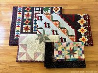 Four folded quilts displayed on hardwood floor showing varied patterns