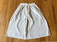 Full view of antique white cotton petticoat laid flat on wooden floor showing gathered waistband and quilted band along bottom hem