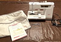 Machine with cover, manual, hoop, sheet, power cord and scissors on table