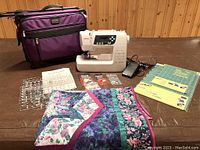All items laid out: machine, suitcase, quilt, cutting guides, needles, bobbins