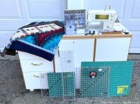 Wide shot of sewing machine on cabinet, folded quilts on left, cutting mats in front