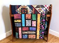 Oak quilt stand holding two quilts against wall