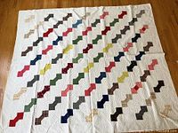 Full view of vintage bow tie quilt laid out flat on wooden floor, showing diagonal bow tie pattern in various colors on white background.