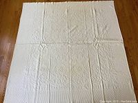 Full view of the vintage cream matelasse coverlet showing overall size and pattern layout on hardwood floor.