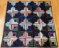 Full view of the Log Cabin quilt with multiple squares made of various colored fabric strips laid out on a wooden floor.