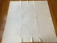 Full view of the cream-colored quilt showing the overall rectangular shape and quilted texture, laid flat on a wooden floor.