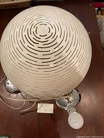 Top and side views of the white spherical hanging light showing the decorative horizontal and curved cut-outs on the shade and the attached cord and metal mounting base with bulb socket.