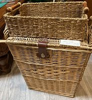 Front view of tall wicker laundry basket with leather strap closure and adjacent rectangular basket
