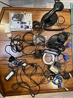 Multiple black cables including VGA, power, USB, with two black handheld barcode scanners with stands on wooden surface