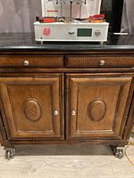Front view of vintage rattan look cabinet with black marble top, two drawers and two doors, on decorative metal wheels.