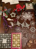 Photo showing various glitter snowflake and floral ornaments, red reindeer antler headband, two boxes of assorted glass and plastic baubles, and peacock feather ornaments.