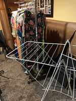 Metal collapsible white drying rack on wheels placed near a clothing rack