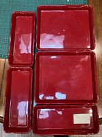 Five thick, glossy red trays arranged on table: three square large trays and two smaller rectangular trays.