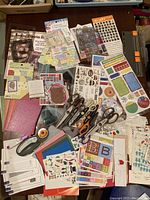Top view of scrapbooking papers, stickers, scissors, and paper cutters spread on a table