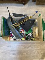 Top view of large bin filled with assorted Lego pieces, baseplates, and a grey pirate ship boat with black sails